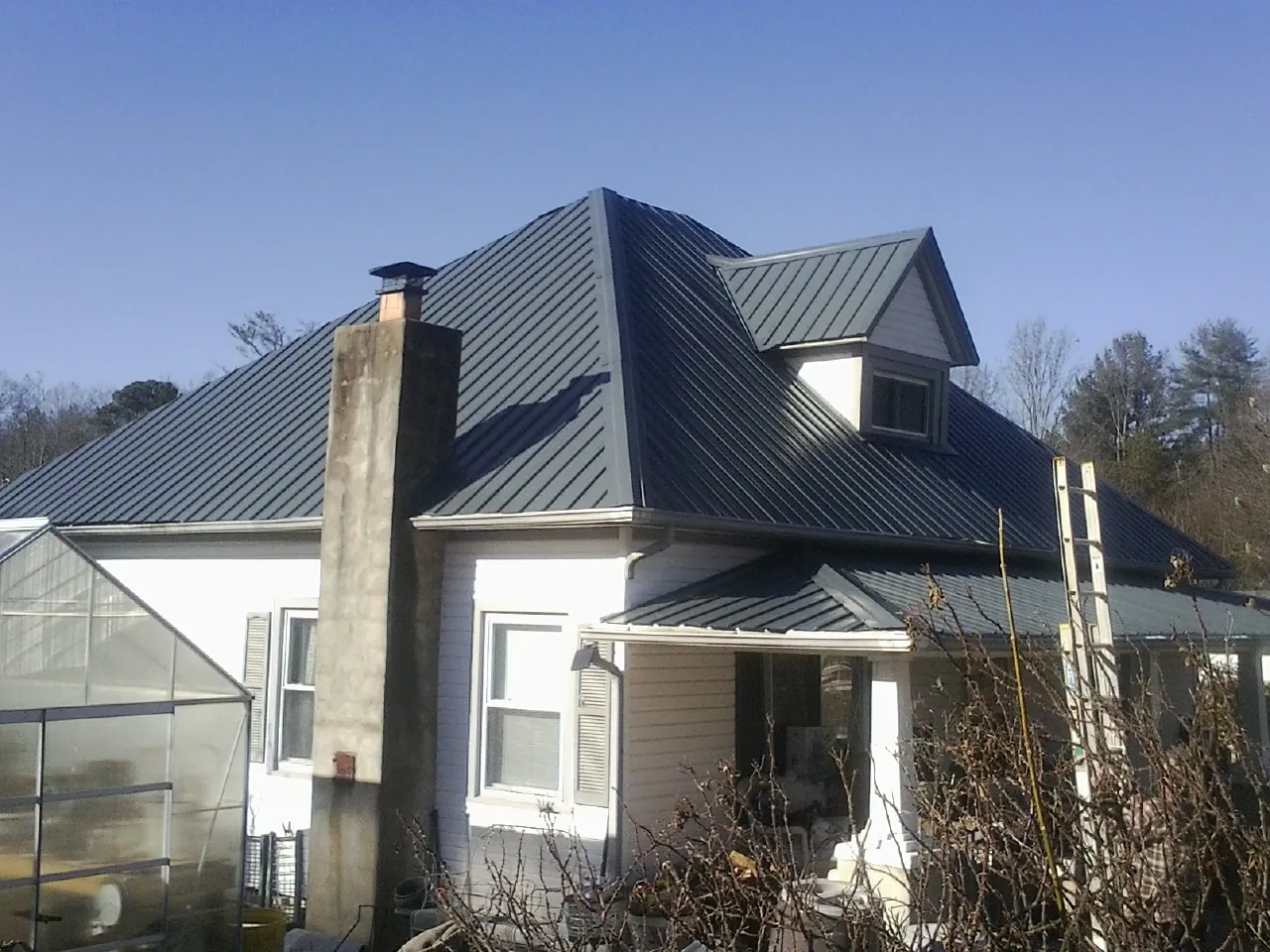 Dark blue standing seam metal roof on a white farmhouse with dormer — Slate & Tile Roof Repair by Roofing Brothers in Anthony