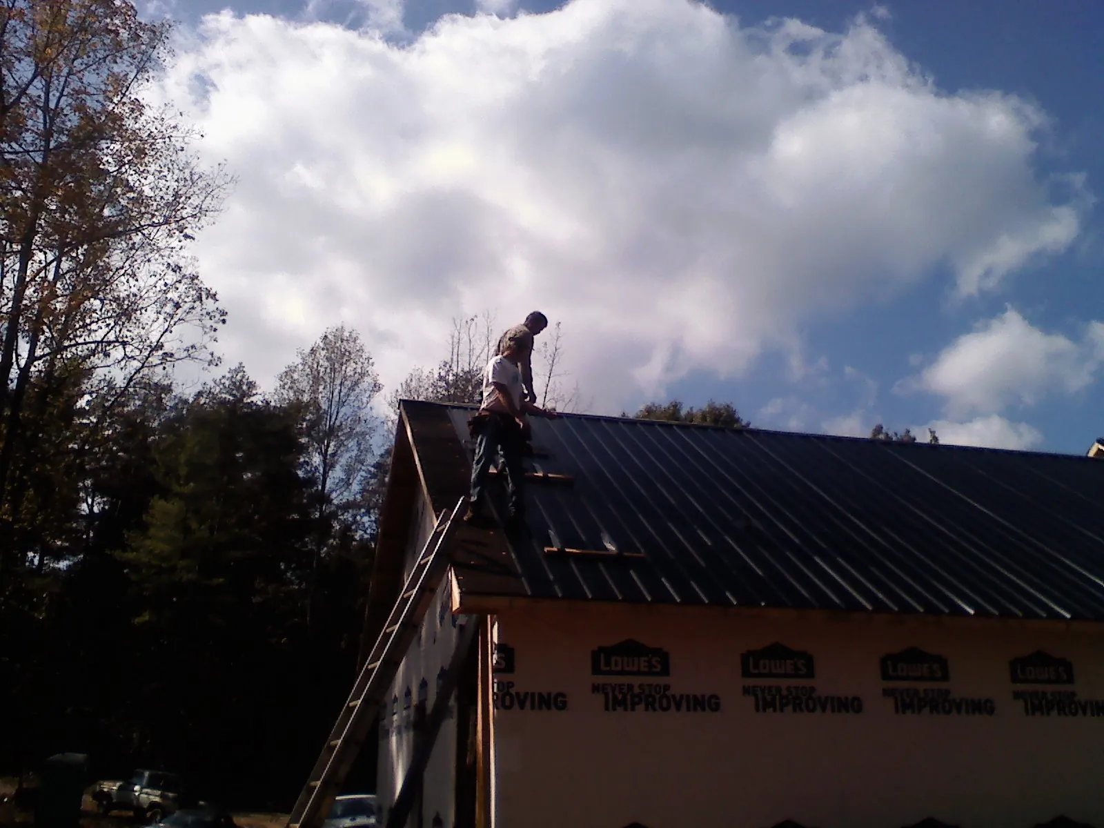 Roofer fastening dark metal panels high against a cloudy sky, from a Roof Inspection job in Anthony
