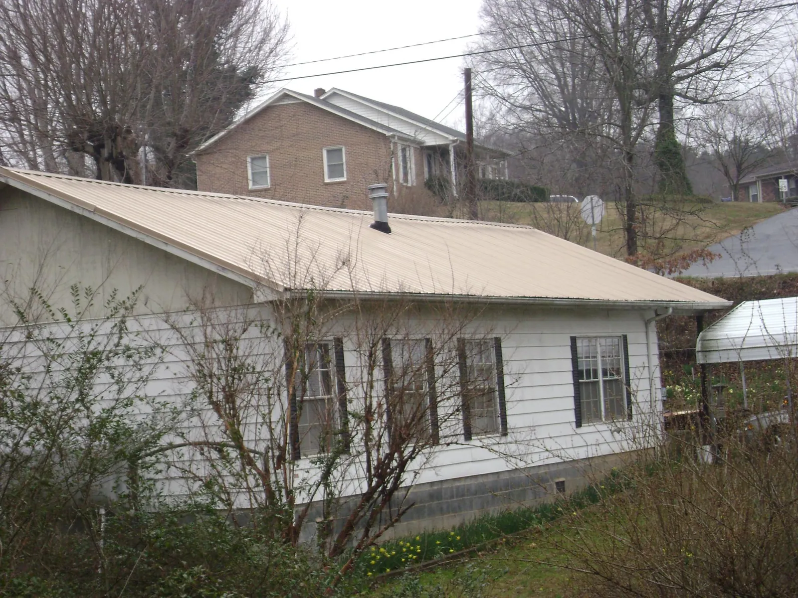 Tan metal roof on a white sided house set into a hillside — Commercial Roofing by Roofing Brothers in Anthony