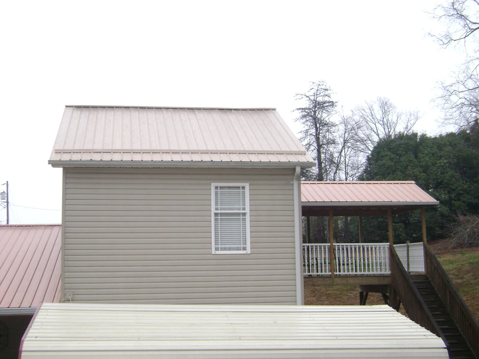 Tan metal roofs on a two story addition and attached porch, from a Roof Replacement job in Anthony